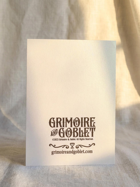 Grimoire and Goblet presents a 5x7 inch pearlescent greeting card. The design features a black linocut-style illustration of an open palm with an eye, surrounded by rays, keys, coins, and stars. The cover reads Luck Fate Fortune and May The Coming Year Favor Your Hand. The interior features a smaller hand icon and a printed blessing. The paper has a luxury silvery shimmer finish.