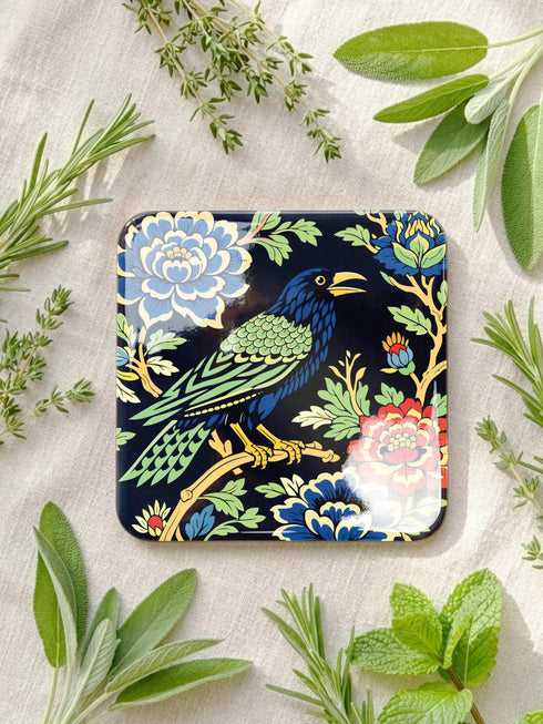 Grimoire and Goblet set of 4 glossy square coasters featuring Chinoiserie style raven illustrations. 1: Navy blue with blue floral pattern and raven. 2: Navy background with black raven, white full moon, and red berries. 3: Moss green background with blue bird and yellow chrysanthemums. 4: Black background with teal-winged raven and red peonies. MDF hardboard with cork backing. Flat vector botanical art style.