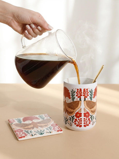 A detailed close-up of a luxury ceramic mug and matching square coaster set from Grimoire and Goblet. The items feature a vintage-style scientific illustration of a large moth with intricate wing patterns in earth tones of rust red and moss green, resting on stylized botanical foliage. The aesthetic is Dark Academia and Victorian Gothic. The mug is a large 15oz white ceramic vessel with a sturdy C-handle. The coaster is a glazed ceramic tile with a glossy finish.
