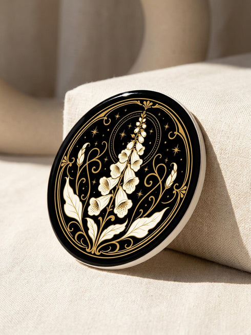 A set of four round 4-inch ceramic coasters featuring a glossy 2D flat-printed Art Deco botanical design. Each coaster displays a different cream-colored flower including a moonflower, foxglove, poppy, and iris, set against a solid black background. The floral motifs are framed by intricate gold linework, crescent moons, four-pointed stars, and mystical symbols like a candle and an all-seeing eye. The coasters have a smooth white edge and are finished with a natural brown cork backing.
