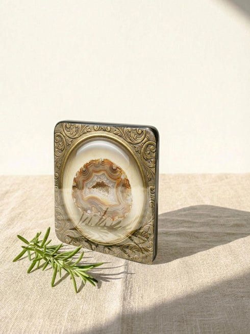 Grimoire and Goblet set of four square glossy coasters featuring high-resolution printed illustrations of raw crystals: purple amethyst, pink rose quartz, iridescent labradorite, and banded agate. Each gemstone is depicted inside a printed faux antique brass baroque frame with intricate scrollwork, set against a cream parchment background. The design is a flat 2D trompe l'œil print on hardboard, creating a realistic 3D specimen box illusion.