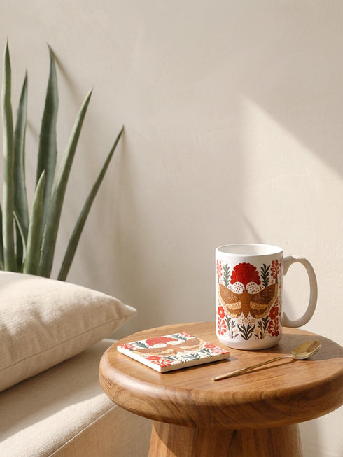 A detailed close-up of a luxury ceramic mug and matching square coaster set from Grimoire and Goblet. The items feature a vintage-style scientific illustration of a large moth with intricate wing patterns in earth tones of rust red and moss green, resting on stylized botanical foliage. The aesthetic is Dark Academia and Victorian Gothic. The mug is a large 15oz white ceramic vessel with a sturdy C-handle. The coaster is a glazed ceramic tile with a glossy finish.
