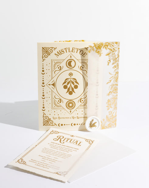 A Grimoire & Goblet luxury Mistletoe ritual card set. The 5x7 cream greeting card features gold celestial designs framing “Mistletoe” and “Love, Protection & New Beginnings.” Shown with a vellum wrap printed in gold florals, a white wax seal with mistletoe, and a premium envelope. Includes a 4x6 ritual insert on handmade deckled paper titled “Ritual for Peace and Protection.” A spiritual Yule stationery set designed as a luxurious unboxing experience.