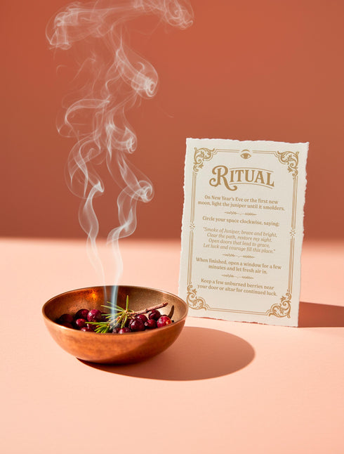 a luxury Grimoire and Goblet ritual card set. A 5x7 cream-colored folded card features an intricate, art-nouveau-style gold foil illustration of a Juniper plant, with the words "Juniper: Cleansing & Fortune." The card is presented with a translucent vellum envelope, which has a gold floral border and a white adhesive wax seal. Inside, the card reveals a vellum-wrapped keepsake, which unfurls to a 4x6 ritual card printed on thick, 160 GSM handmade cotton paper with a rough, deckled edge.