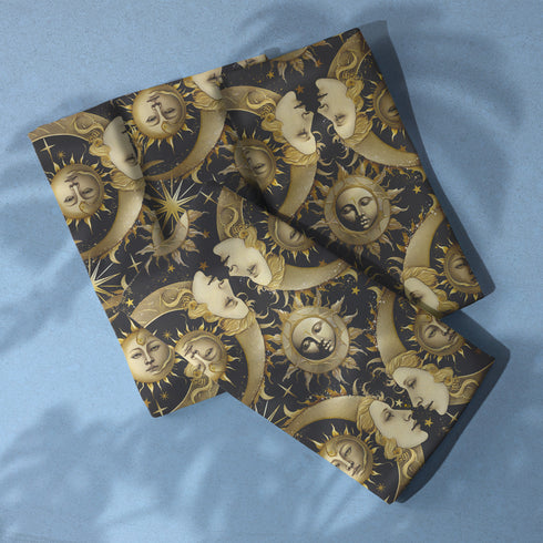 Set of four black cloth napkins with a repeating pattern of golden sun and moon faces, surrounded by swirling flames, craters, and scattered stars.