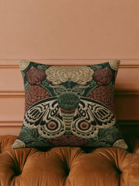 Square 17 by 18 inch jacquard woven throw pillow, woven identically on both faces and closed with a clean sewn edge. A symmetrical emperor moth with wings detailed in black, warm gold, and deep burgundy red spreads across the center of a dark forest green ground. A large golden yellow flower blooms above the moth and burgundy floral buds sit on either side among woven botanical sprays. The design is woven flat into the cotton blend cloth with visible thread texture.