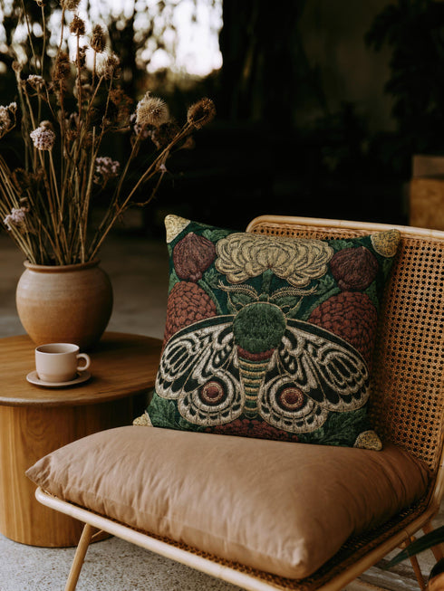 Square 17 by 18 inch jacquard woven throw pillow, woven identically on both faces and closed with a clean sewn edge. A symmetrical emperor moth with wings detailed in black, warm gold, and deep burgundy red spreads across the center of a dark forest green ground. A large golden yellow flower blooms above the moth and burgundy floral buds sit on either side among woven botanical sprays. The design is woven flat into the cotton blend cloth with visible thread texture.