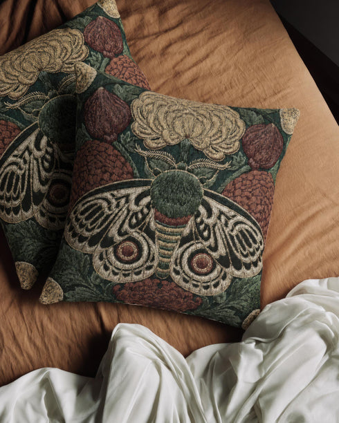 Square 17 by 18 inch jacquard woven throw pillow, woven identically on both faces and closed with a clean sewn edge. A symmetrical emperor moth with wings detailed in black, warm gold, and deep burgundy red spreads across the center of a dark forest green ground. A large golden yellow flower blooms above the moth and burgundy floral buds sit on either side among woven botanical sprays. The design is woven flat into the cotton blend cloth with visible thread texture.