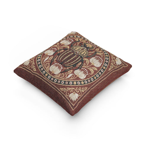 Square 17 by 18 inch jacquard woven throw pillow, woven identically on both faces and closed with a clean finished edge. A large detailed scarab beetle in black, gold, and dark brown sits at the center inside a dotted circular border, surrounded by symmetrical Art Nouveau vines and cream lotus flowers on a rust red ground. Small white floral motifs sit in each corner. The design is woven flat into the cotton blend cloth, with visible thread texture and a soft sheen in the ground.