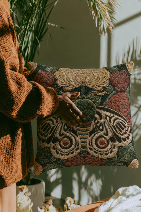 Square 17 by 18 inch jacquard woven throw pillow, woven identically on both faces and closed with a clean sewn edge. A symmetrical emperor moth with wings detailed in black, warm gold, and deep burgundy red spreads across the center of a dark forest green ground. A large golden yellow flower blooms above the moth and burgundy floral buds sit on either side among woven botanical sprays. The design is woven flat into the cotton blend cloth with visible thread texture.