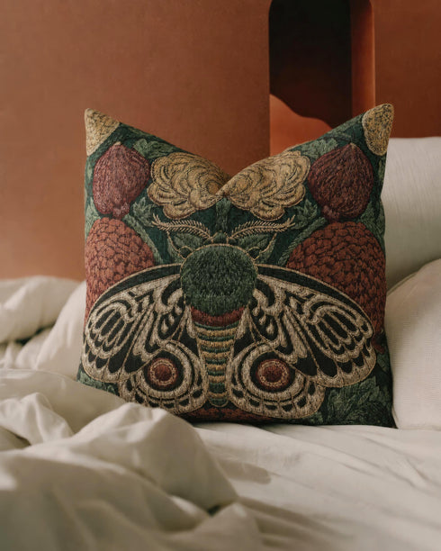Square 17 by 18 inch jacquard woven throw pillow, woven identically on both faces and closed with a clean sewn edge. A symmetrical emperor moth with wings detailed in black, warm gold, and deep burgundy red spreads across the center of a dark forest green ground. A large golden yellow flower blooms above the moth and burgundy floral buds sit on either side among woven botanical sprays. The design is woven flat into the cotton blend cloth with visible thread texture.