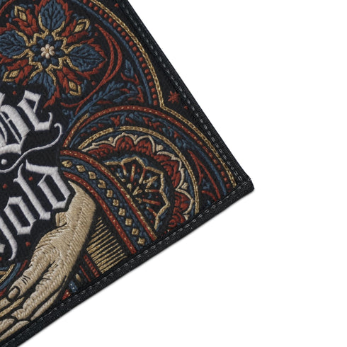 Rectangular navy doormat with a low loop polyester pile and black border trim, printed flat to imitate hand embroidery and crewelwork. Two pale hands offer a golden chalice at the center, with white rays streaming from the cup. Ornate white lettering across the design reads BLESSED BE THE THRESHOLD. Rust red and antique gold Arts and Crafts botanical arches frame the scene, curving over and around the chalice against the deep navy ground.