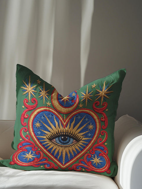 Square pillow cover in smooth linen-like polyester with a concealed zipper, printed on both faces to imitate hand embroidery and tapestry, with no stitching or raised texture. On an emerald green field, a cobalt blue heart holds an open eye with an azure iris at the center. A golden crescent moon, sunburst rays, and small stars shine above the heart. Scarlet acanthus scrollwork frames the heart, with golden cord detailing and starburst medallions in each corner.