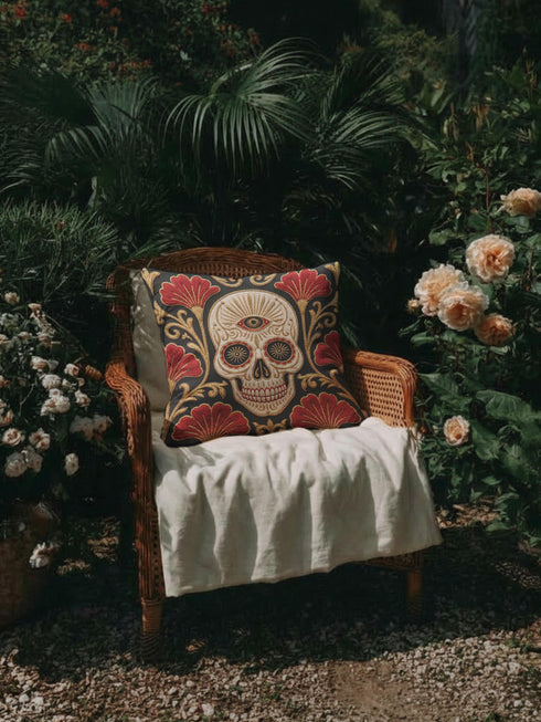 Square pillow cover in smooth linen-like polyester with a concealed bottom zipper, printed on both faces to imitate hand embroidery and tapestry, with no stitching or raised texture. On a charcoal black ground, an ivory skull carries an open radiating third eye on its brow, with golden starbursts glowing in its eye sockets. Crimson fan shaped botanical blooms spread around the skull, framed by antique gold acanthus scrollwork that curls toward each corner of the cover.