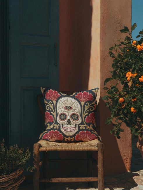 Square pillow cover in smooth linen-like polyester with a concealed bottom zipper, printed on both faces to imitate hand embroidery and tapestry, with no stitching or raised texture. On a charcoal black ground, an ivory skull carries an open radiating third eye on its brow, with golden starbursts glowing in its eye sockets. Crimson fan shaped botanical blooms spread around the skull, framed by antique gold acanthus scrollwork that curls toward each corner of the cover.