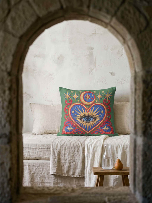 Square pillow cover in smooth linen-like polyester with a concealed zipper, printed on both faces to imitate hand embroidery and tapestry, with no stitching or raised texture. On an emerald green field, a cobalt blue heart holds an open eye with an azure iris at the center. A golden crescent moon, sunburst rays, and small stars shine above the heart. Scarlet acanthus scrollwork frames the heart, with golden cord detailing and starburst medallions in each corner.