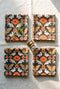 Set of four square cloth dinner napkins, each 20 by 20 inches, in polyester broadcloth with hemmed edges. The top face is printed with a mirrored damask style pattern of golden luna moths, burnt orange poppies, small coral blossoms, and ivory acanthus scrollwork on a solid black ground. The underside is white and shows a faint, softened echo of the printed pattern through the lightweight, smooth, densely woven fabric.