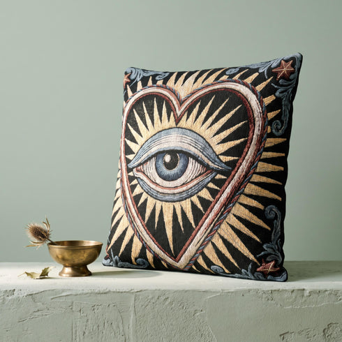 Square 17 by 18 inch jacquard woven throw pillow, woven identically on both faces and closed with a clean finished edge. On a solid black ground, a large blue evil eye sits inside a golden sunburst heart. Gold, pale blue, cream, and rust threads form the design, with dusty blue acanthus leaves curling around the heart and small rust stars in each corner. The design is woven flat into the cotton blend cloth, with visible thread texture and a heavy tapestry hand.