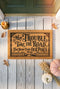 Rectangular natural tan coir doormat, 24 by 16 inches, with squared corners, a bristled tufted coconut fiber surface, and a black vinyl backing. The black artwork is printed into the fibers inside a double line frame. Ornate Victorian lettering reads MAY TROUBLE TAKE THE ROAD THAT NEVER FINDS OUR PORCH. Turned porch posts with scrolled corner brackets stand on each side, a row of balusters runs along the bottom, and a small winding road and magnolia blossom sit at the center.
