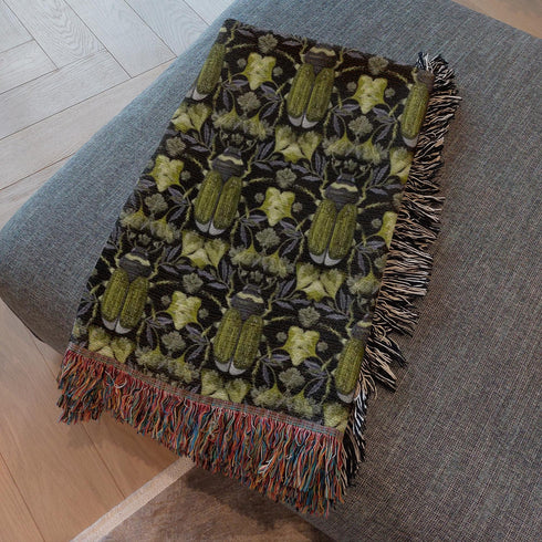 Luxurious woven cotton throw blanket featuring symmetrical scarab beetle pattern in olive green on black background with white fringe trim. Perfect for dark academia, gothic, or cottagecore decor as wall hanging or cozy throw. Mystical home gift.