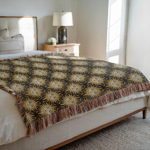 A woven cotton throw featuring a celestial sun face pattern in gold and black tones, framed by soft fringe.